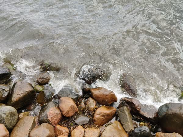 An aerial shot of wave crashing on a shingle beach.
